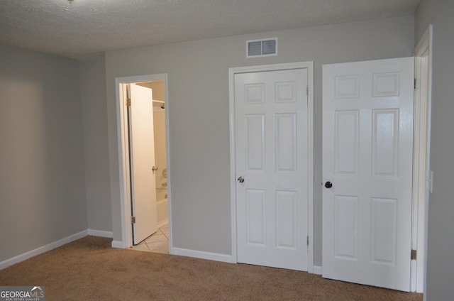 unfurnished bedroom with visible vents, light colored carpet, a textured ceiling, and baseboards