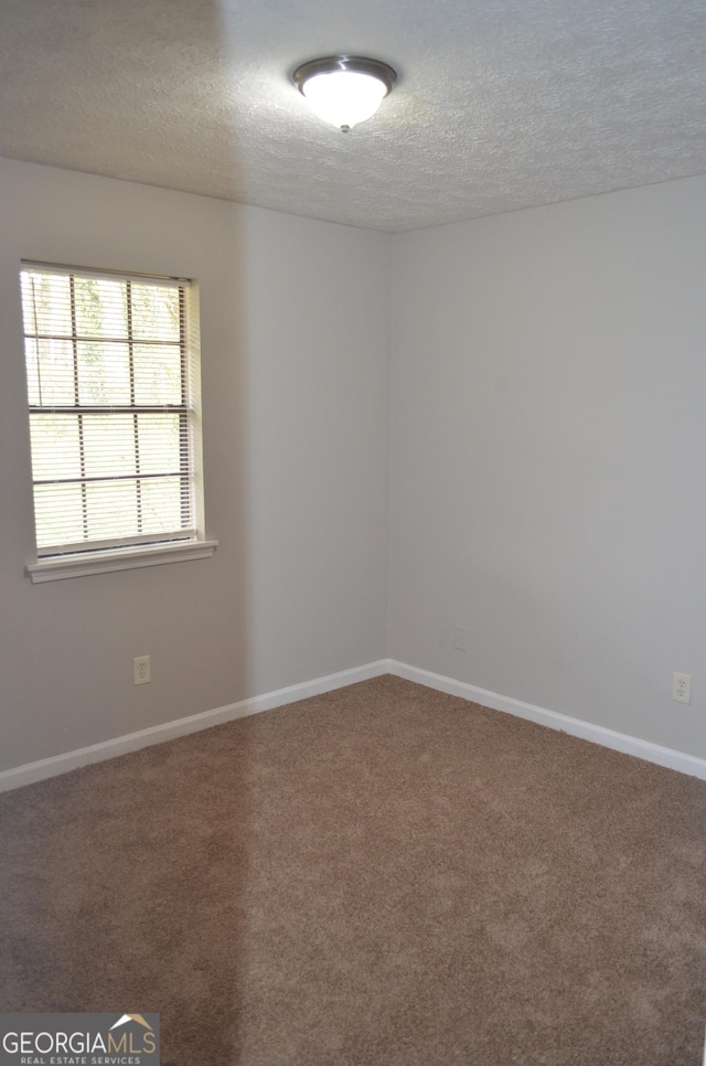 empty room featuring carpet flooring, a textured ceiling, and baseboards