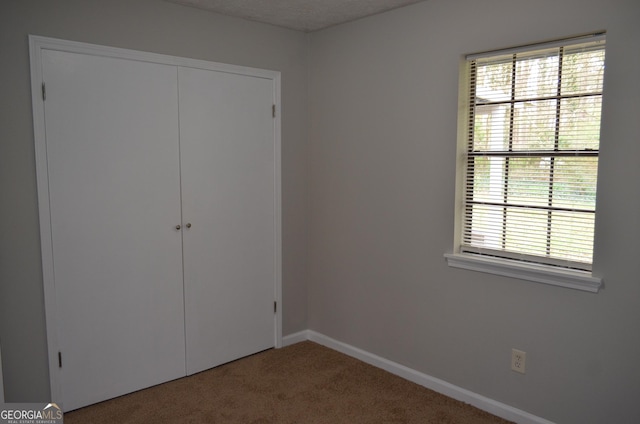 unfurnished bedroom featuring multiple windows, carpet, a closet, and baseboards