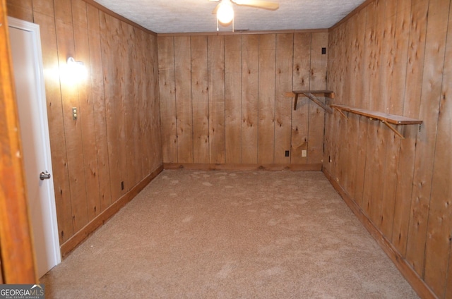 empty room with a ceiling fan, wood walls, carpet flooring, and a textured ceiling