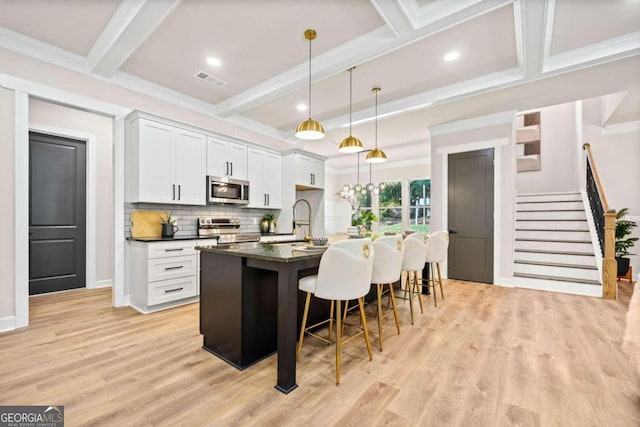 kitchen featuring a kitchen island with sink, appliances with stainless steel finishes, dark countertops, a kitchen breakfast bar, and tasteful backsplash