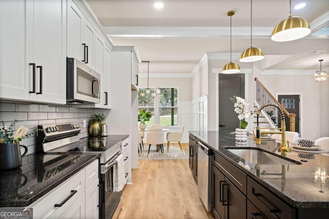 kitchen with appliances with stainless steel finishes, light wood-type flooring, crown molding, and a sink