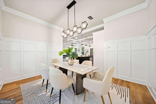 dining area featuring wood finished floors, ornamental molding, and a decorative wall