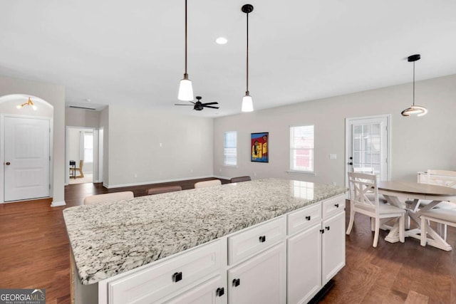 kitchen featuring light stone counters, a ceiling fan, dark wood-style flooring, hanging light fixtures, and white cabinetry