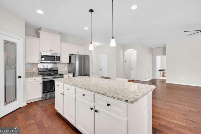 kitchen with dark wood finished floors, a center island, arched walkways, and stainless steel appliances