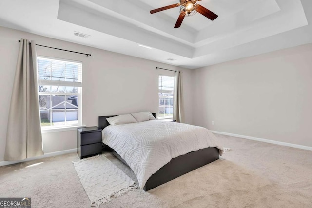 carpeted bedroom featuring baseboards, a raised ceiling, visible vents, and a ceiling fan