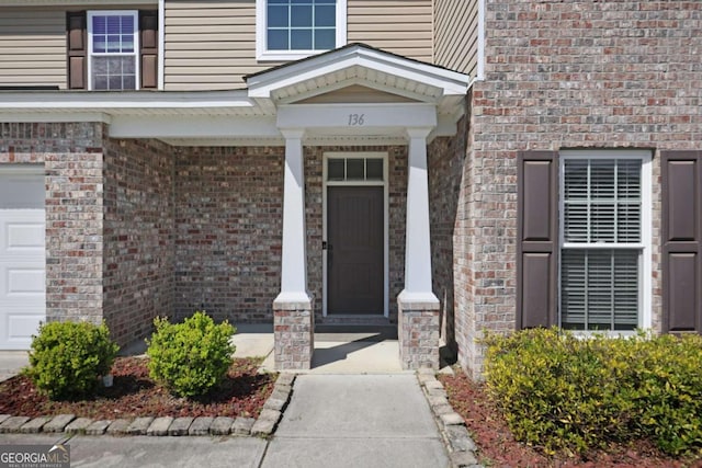 doorway to property with brick siding, a porch, and a garage