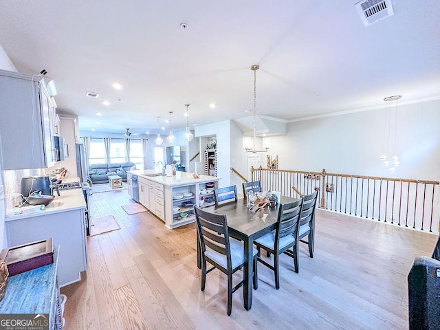 dining area with visible vents, ceiling fan with notable chandelier, light wood-type flooring, and ornamental molding