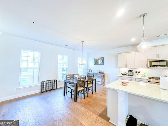 kitchen with stainless steel microwave, light wood-style flooring, light countertops, and decorative backsplash