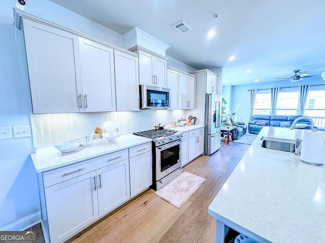 kitchen with visible vents, a sink, stainless steel appliances, light wood-style floors, and white cabinetry