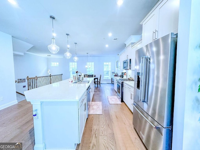 kitchen with an island with sink, light wood-style flooring, appliances with stainless steel finishes, white cabinetry, and a sink