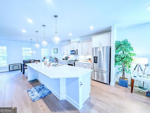 kitchen featuring a sink, light wood-style flooring, stainless steel appliances, white cabinetry, and a kitchen island with sink