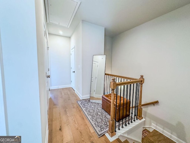 hall with attic access, light wood-style flooring, an upstairs landing, and baseboards