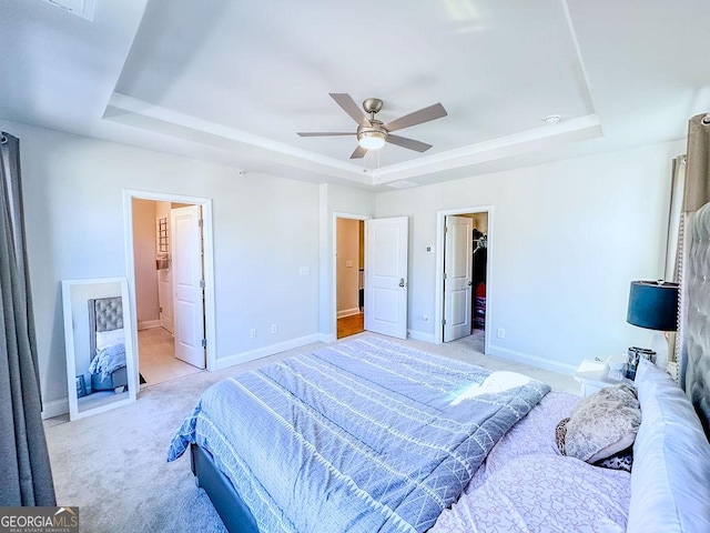 bedroom featuring a tray ceiling, baseboards, light colored carpet, and a spacious closet