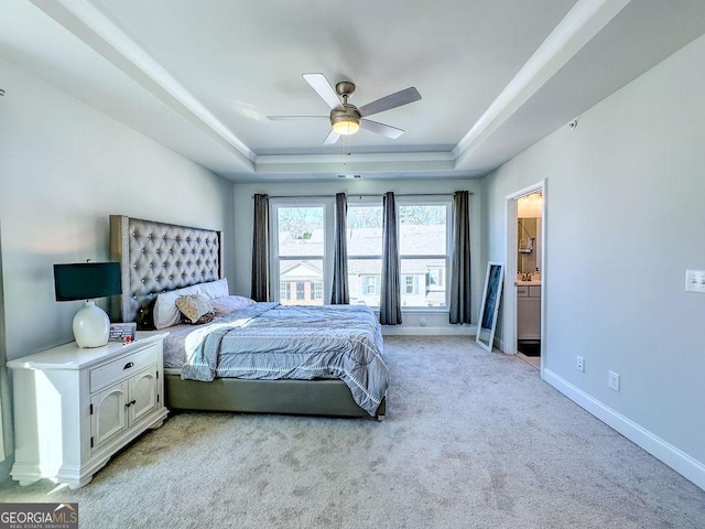 bedroom featuring baseboards, light colored carpet, ensuite bath, a raised ceiling, and a ceiling fan