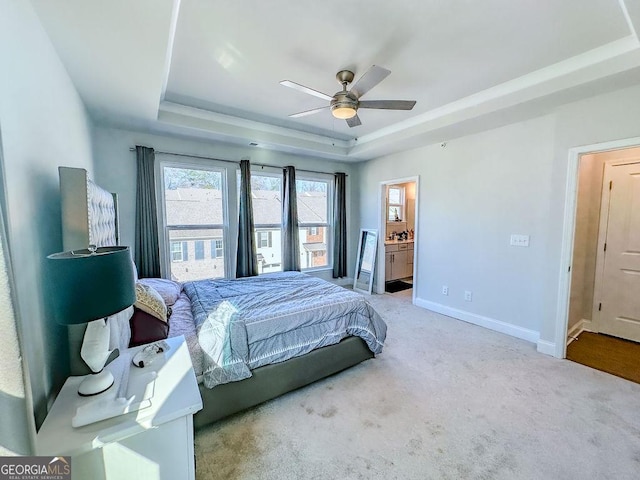 bedroom with carpet flooring, baseboards, ensuite bathroom, and a tray ceiling