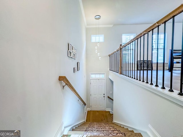 stairs with a towering ceiling, crown molding, baseboards, and wood finished floors