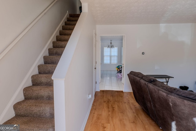 staircase with a chandelier, a textured ceiling, and wood finished floors