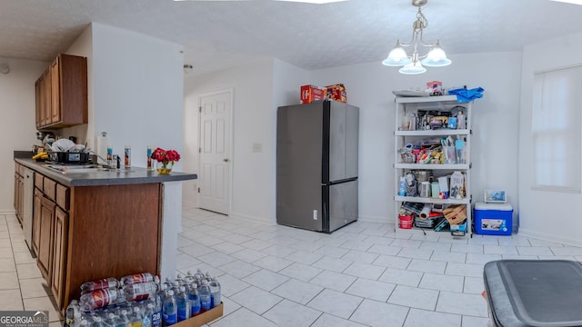 kitchen featuring freestanding refrigerator, a sink, a textured ceiling, dark countertops, and brown cabinets