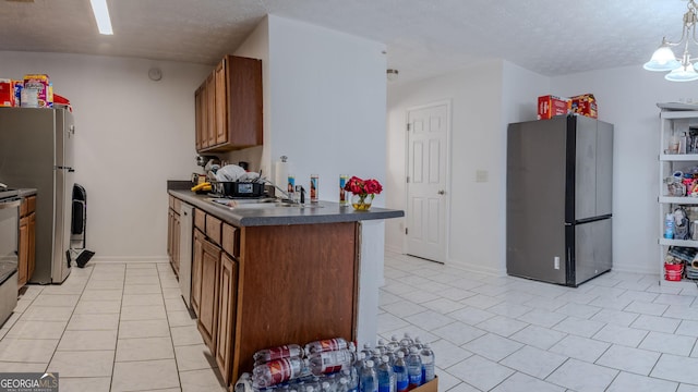 kitchen featuring dark countertops, brown cabinetry, freestanding refrigerator, and a sink