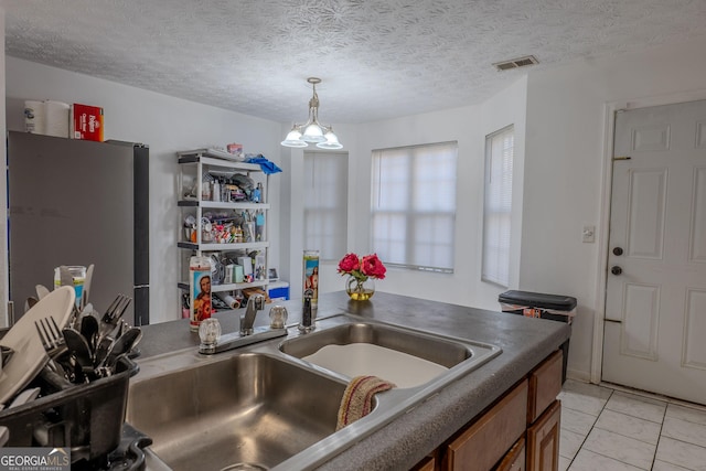 kitchen featuring dark countertops, visible vents, freestanding refrigerator, brown cabinetry, and a sink