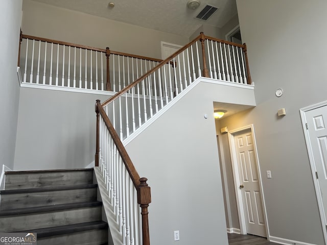 stairs with visible vents, baseboards, and a towering ceiling