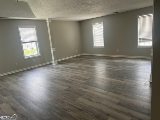 spare room with baseboards, a textured ceiling, ornate columns, and dark wood-style flooring