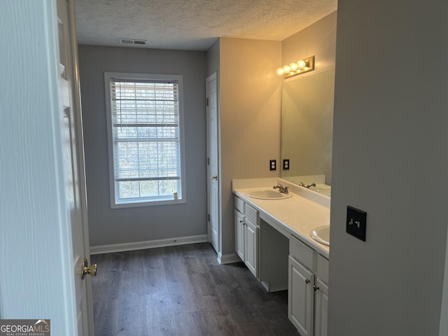 bathroom with visible vents, double vanity, wood finished floors, a textured ceiling, and a sink