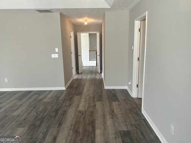 hall with visible vents, baseboards, dark wood-style flooring, and a textured ceiling