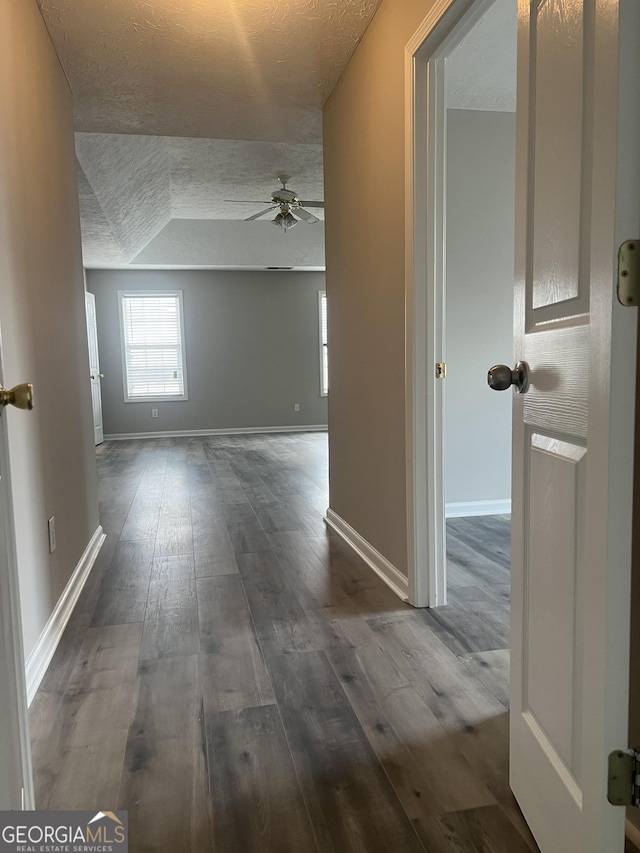 corridor with a textured ceiling, baseboards, and dark wood-style flooring