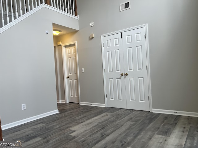 interior space with visible vents, dark wood-type flooring, baseboards, and a towering ceiling