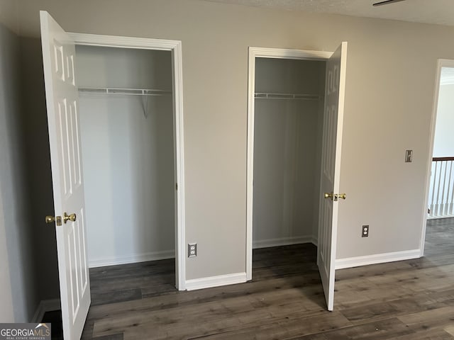 unfurnished bedroom featuring two closets, baseboards, and wood finished floors