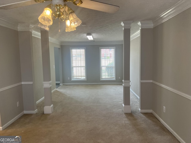 carpeted empty room with a textured ceiling, crown molding, baseboards, and decorative columns