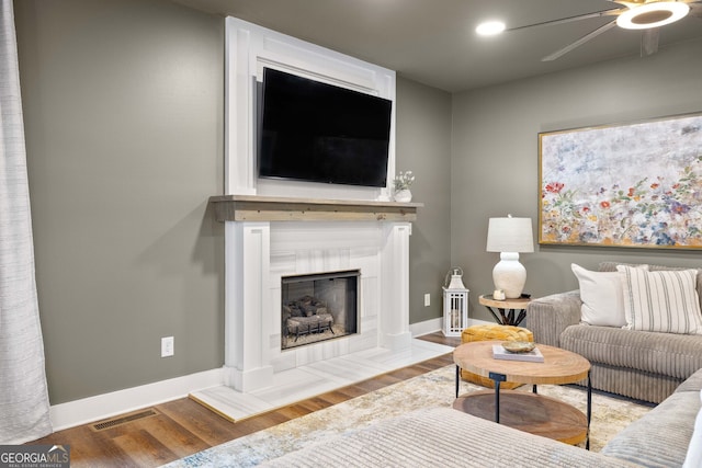 living room featuring visible vents, baseboards, ceiling fan, a tiled fireplace, and wood finished floors