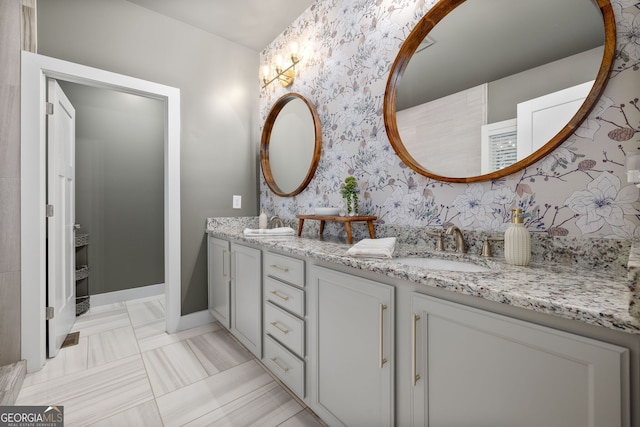 bathroom with wallpapered walls, double vanity, baseboards, and a sink