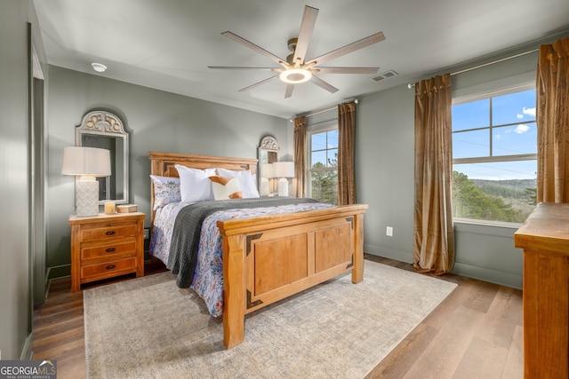 bedroom featuring ceiling fan, visible vents, baseboards, and wood finished floors