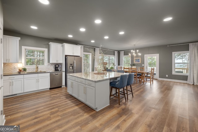 kitchen with a sink, appliances with stainless steel finishes, white cabinetry, a kitchen breakfast bar, and a center island