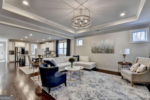 living room with baseboards, a tray ceiling, ornamental molding, dark wood-type flooring, and a notable chandelier