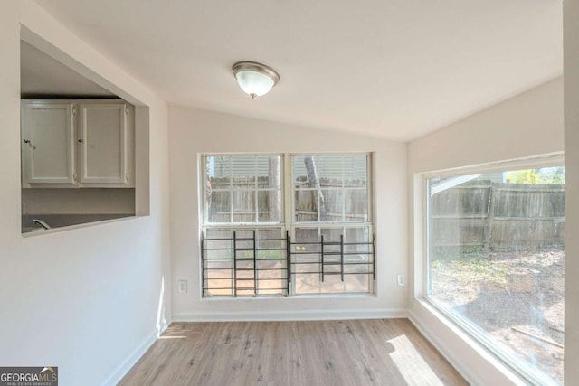 unfurnished dining area featuring baseboards, lofted ceiling, and light wood finished floors