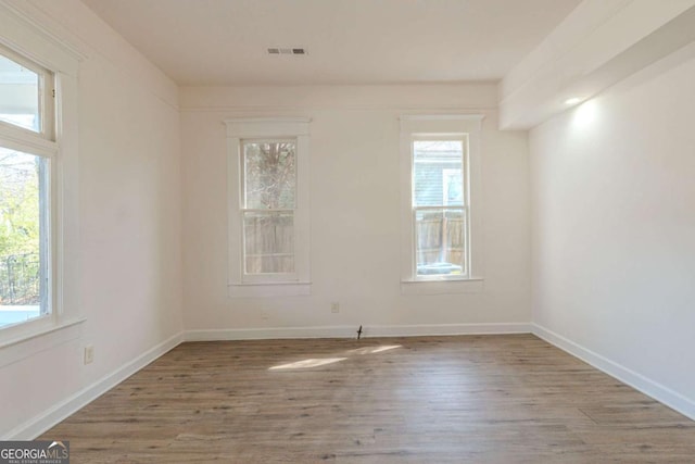 unfurnished room featuring baseboards, wood finished floors, visible vents, and a healthy amount of sunlight