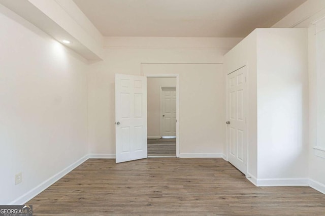 unfurnished bedroom featuring wood finished floors, baseboards, and a closet