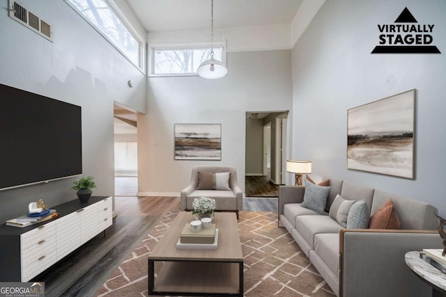 living area featuring a high ceiling, a skylight, wood finished floors, and visible vents