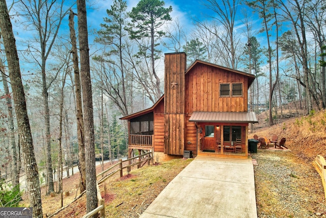 chalet / cabin featuring board and batten siding, covered porch, concrete driveway, metal roof, and a chimney