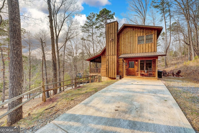 chalet / cabin with a chimney, covered porch, board and batten siding, and metal roof