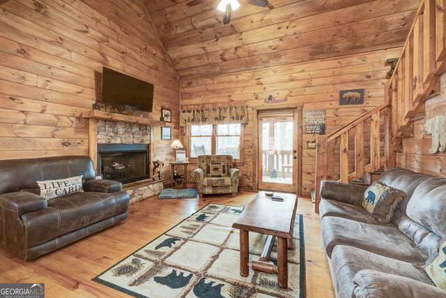 living room featuring high vaulted ceiling, wood finished floors, wooden walls, a stone fireplace, and stairs