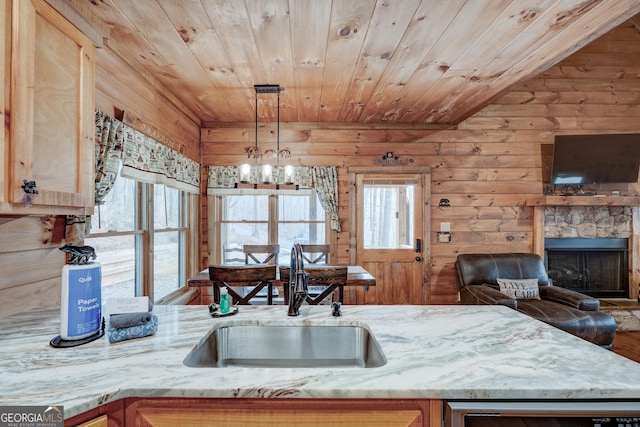 kitchen featuring a sink, wooden ceiling, open floor plan, light stone counters, and wood walls