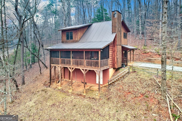 exterior space featuring a forest view, metal roof, a chimney, and a sunroom