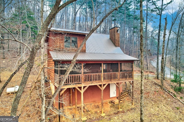 rear view of property with a sunroom, a chimney, metal roof, and stairway