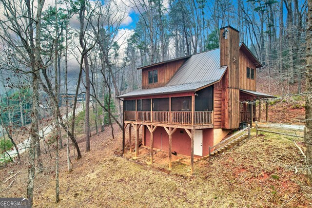 rear view of house with a sunroom, a chimney, metal roof, and a deck