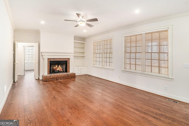 unfurnished living room featuring visible vents, ornamental molding, a ceiling fan, wood finished floors, and a fireplace